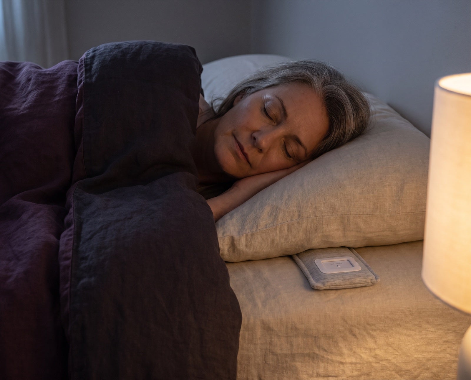 A woman settled and asleep in lamplight, the Drowsie speaker under her pillow